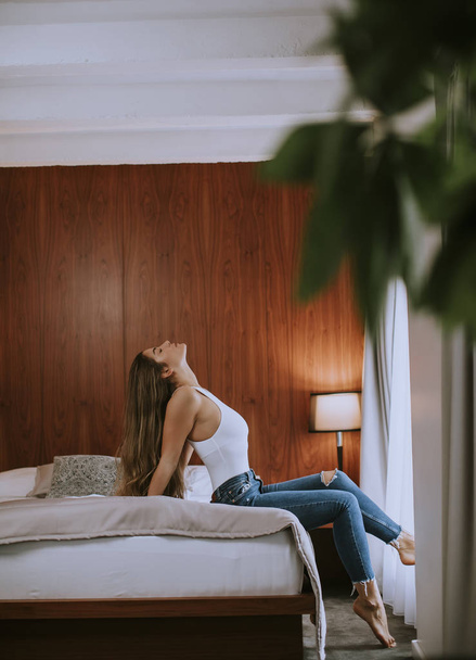 Mulher bonita em calças jeans elegantes sentado na cama em casa
 - Foto, Imagem