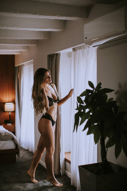 Beautiful young woman in lingerie looking outside the window in her beautiful apartment - Foto, Imagen