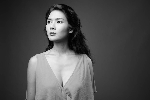 Зйомки прекрасної азіатської жінки в одязі проти сірого фону в чорно-білому - Фото, зображення