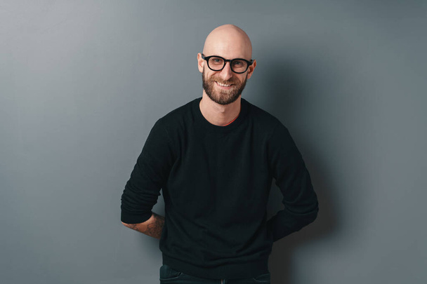 Giovane uomo sorridente con barba e occhiali su sfondo grigio studio
 - Foto, immagini