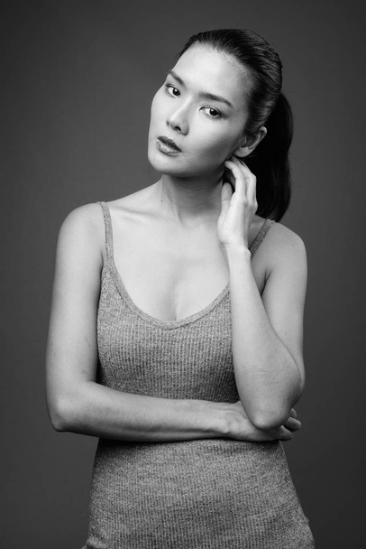Studio shot of beautiful Asian woman wearing sleeveless dress against gray background in black and white - Photo, image