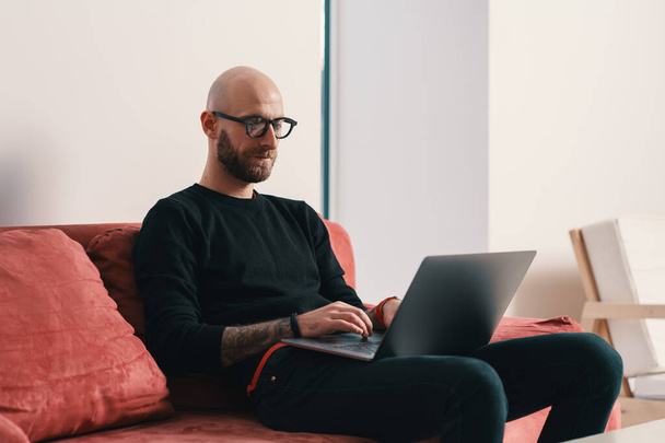 Modern young caucasian man with beard and glasses relaxing while surfing internet on laptop pc - Fotografie, Obrázek