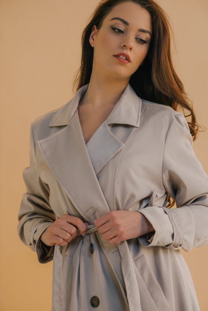 Low angle view of attractive girl in coat looking away isolated on beige - Fotó, kép