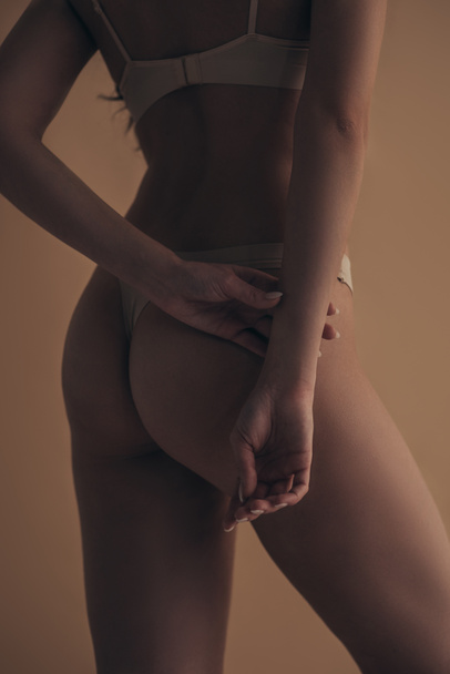 Вид сзади на сексуальную женщину в нижнем белье изолированный на бежевом, обрезанный вид
 - Фото, изображение
