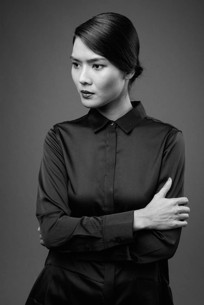 Studio shot of beautiful Asian businesswoman wearing black shirt against gray background in black and white - Valokuva, kuva