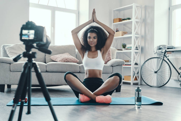 Beautiful young African woman sitting in the yoga while making social media video                   - Foto, imagen