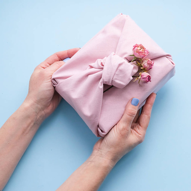 Naisten kädet tilalla loma lahja pakattu kangas tavalla Furoshiki muodikas sininen tausta
. - Valokuva, kuva