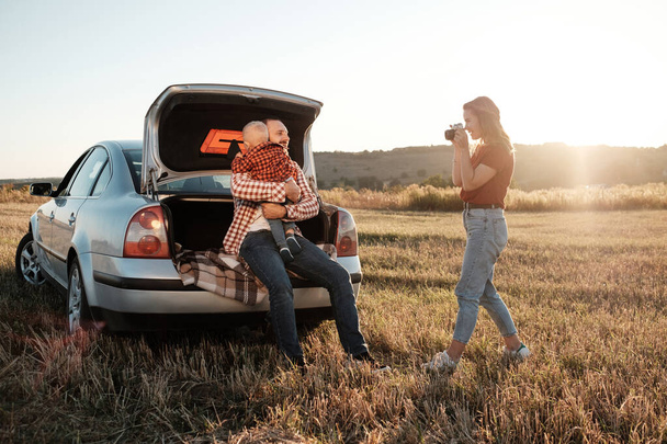 Happy Young Family Mom and Dad with Their Little Son Enjoying Summer Weekend Picnic on the Car Outside the City in the Field at Sunny Day Sunset, Vacation and Road Trip Concept - Photo, Image