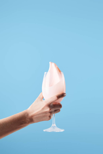 青で隔離された新鮮なピンクのミルクスプラッシュとガラスを保持する女性のクロップドビュー - 写真・画像