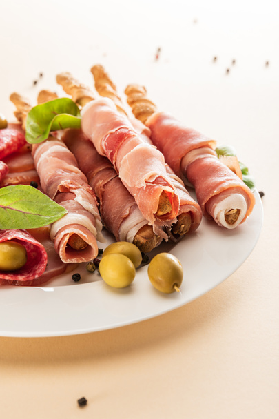 delicious meat platter served with olives and breadsticks on plate on beige background - Zdjęcie, obraz