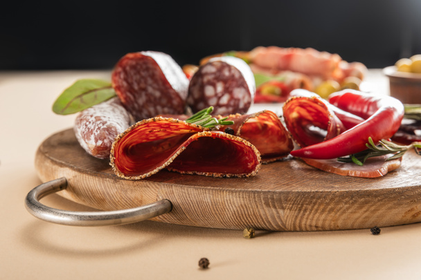ベージュの木の板にローズマリーと唐辛子を盛り付けた美味しいお肉の盛り合わせ - 写真・画像
