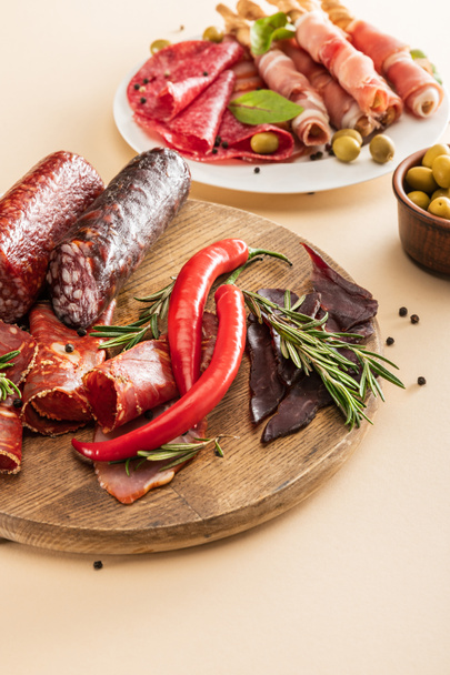 вкусные мясные блюда с оливками, специями и хлебными палочками на тарелке и деревянной доской на бежевом фоне
 - Фото, изображение
