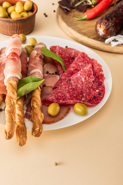 herkullisia lihatarjottimia tarjoillaan oliivien, mausteiden ja leipätikkujen kanssa lautasella ja puulaudalla beige taustalla
 - Valokuva, kuva