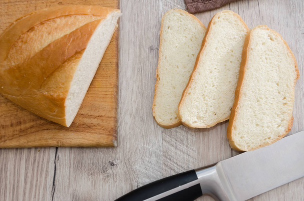 μακρύ καρβέλι σε ξύλινη σανίδα και μαχαίρι. Υπέροχο Ουκρανικό ψωμί. Κομμένο άσπρο ψωμί. - Φωτογραφία, εικόνα