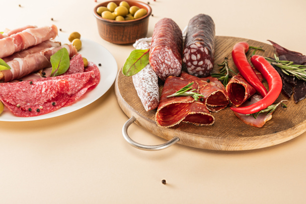 heerlijke vleesschotels geserveerd met olijven, specerijen op bord en houten bord op beige achtergrond - Foto, afbeelding