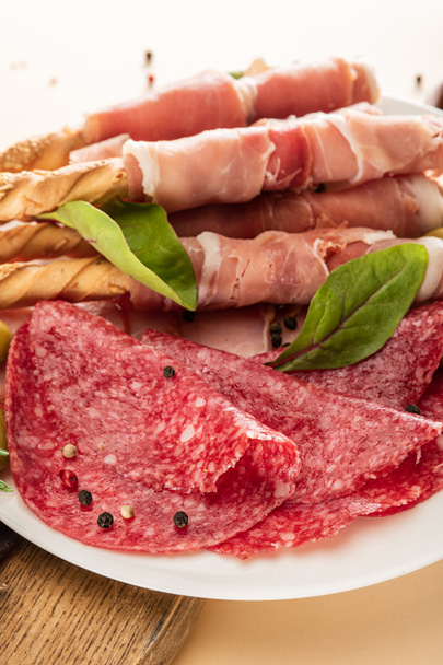köstliche Fleischplatte serviert mit Oliven, Gewürzen und Semmelstangen auf Teller auf beigem Hintergrund - Foto, Bild