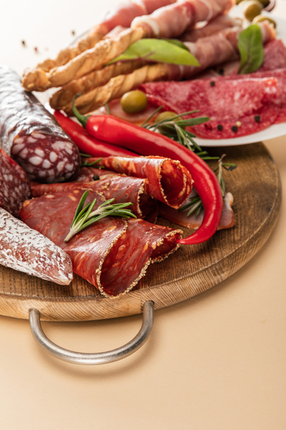 вкусные мясные блюда с оливками, специями и хлебными палочками на тарелке и деревянной доской на бежевом фоне
 - Фото, изображение