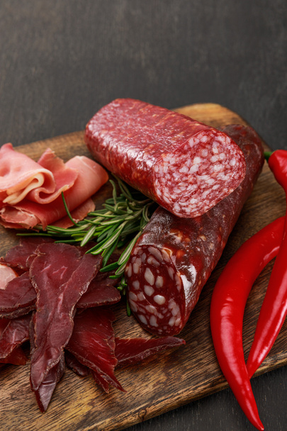 Nahsicht auf köstliche Fleischplatte mit Chili und Rosmarin auf schwarzem Holztisch - Foto, Bild