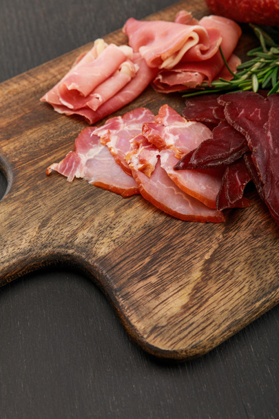 close up view of delicious meat platter served with rosemary on wooden black table - Foto, imagen