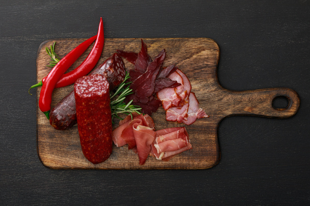 Ahşap masa üzerinde kırmızı biber ve biberiyeyle servis edilen lezzetli et tabağının üst görüntüsü. - Fotoğraf, Görsel