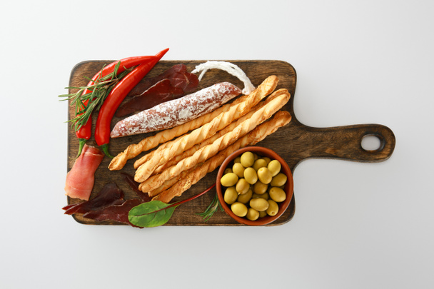 Blick von oben auf köstliche Fleischplatte serviert mit Semmelstangen, Oliven, Chilischoten und Kräutern an Bord isoliert auf weiß - Foto, Bild