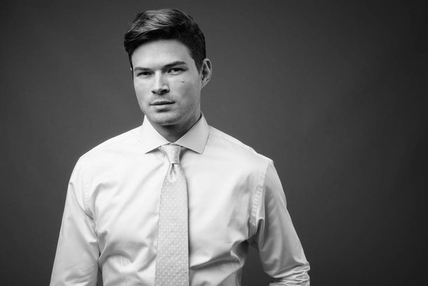 Studio shot of young handsome businessman against gray background - Foto, afbeelding