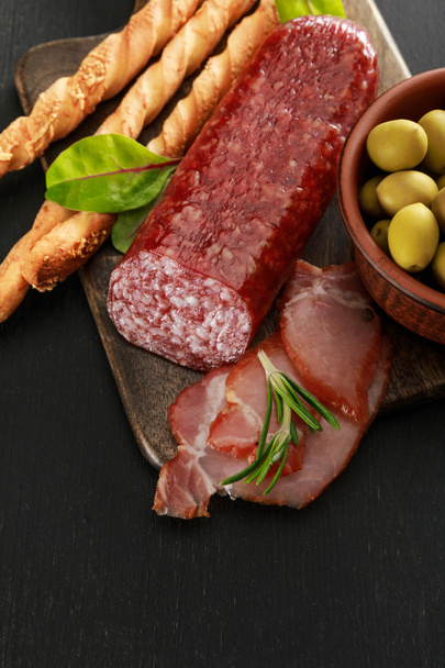 delicious meat platter served with olives and grissini on board on black surface - Photo, Image