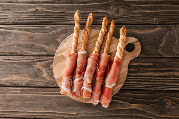 bovenaanzicht van heerlijke vleesschotel met broodstokjes en prosciutto op houten plank - Foto, afbeelding