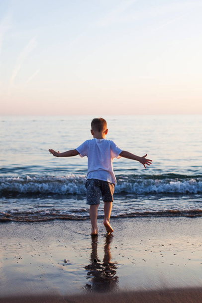 A little boy runs along a sandy beach in the sea at sunset. - Photo, Image