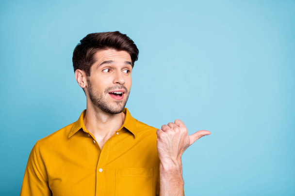 Photo of brown haired businessman pointing at empty space with thumb notifying important information with surprised facial expression isolated blue pastel color background - Photo, image