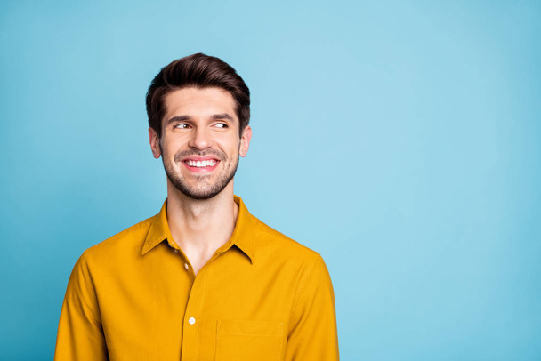 Photo of cheerful nice creative young guy freelancer in yellow shirt looking into empty space smiling toothily isolated over blue pastel color background - Fotó, kép