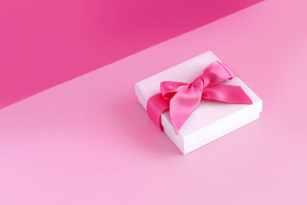 Bílá dárková krabice s lukem na světle růžovém pozadí - Fotografie, Obrázek