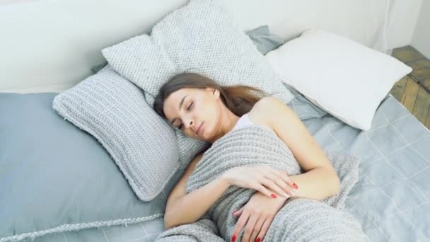 Young attractive woman waking up in bed. The concept of rest and healthy sleep - Záběry, video