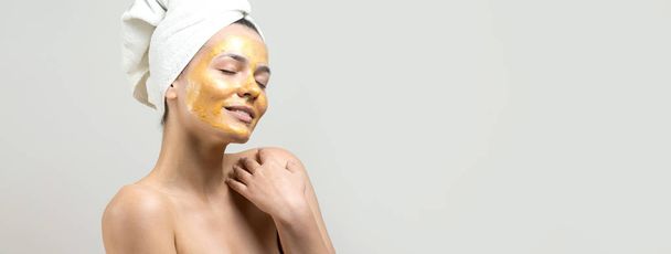 Schönheitsporträt einer Frau in weißem Handtuch auf dem Kopf mit goldener Pflegemaske im Gesicht. Reinigung der Haut Öko-Kosmetik Wellness-Entspannungskonzept. - Foto, Bild