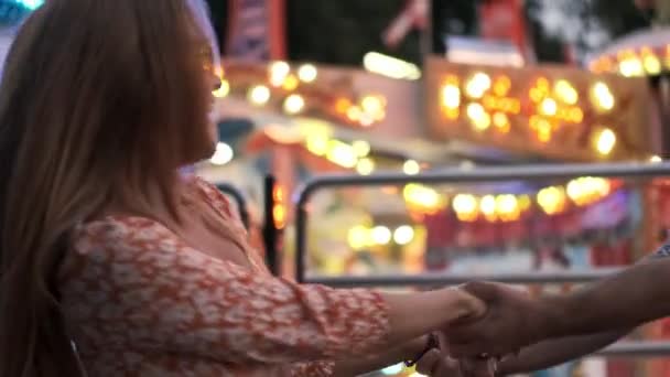 Glücklich lächelndes junges Paar, Mann und Frau wirbeln Händchen haltend in einem Vergnügungspark - Filmmaterial, Video