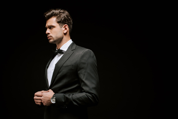elegant man in suit looking away isolated on black  - Foto, imagen
