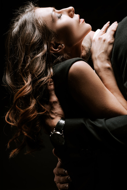 άνδρας αγκαλιάζει και φιλάει γυναίκα με κλειστά μάτια απομονωμένη σε μαύρο  - Φωτογραφία, εικόνα