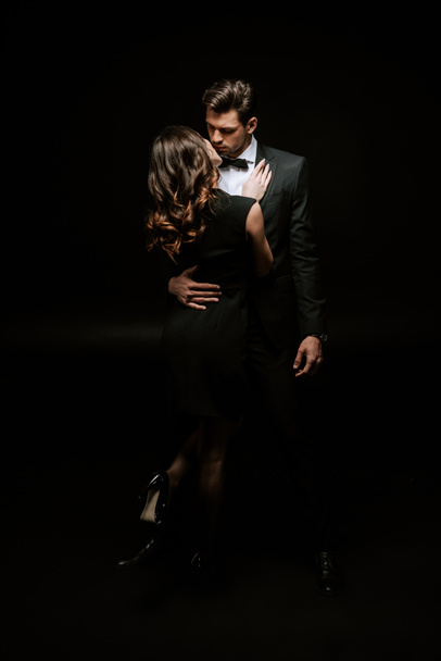 woman hugging handsome man in suit on black  - Foto, afbeelding
