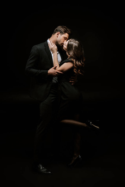 woman kissing handsome man in suit isolated on black  - Fotó, kép