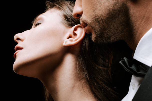 recortado vista de hombre cerca sensual chica con los ojos cerrados aislado en negro
  - Foto, Imagen