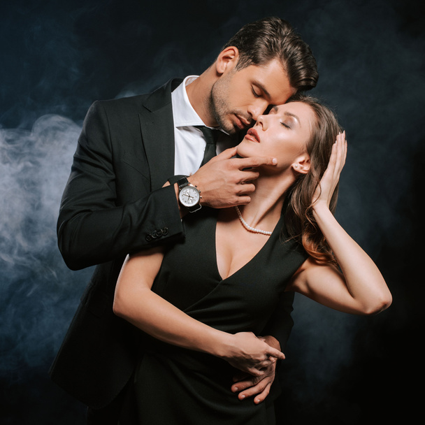 handsome man touching attractive woman in dress on black with smoke  - Photo, Image