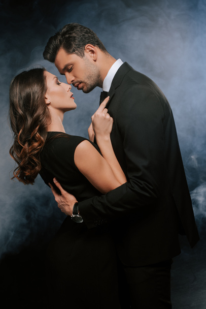 side view of man hugging attractive woman on black with smoke  - Photo, Image