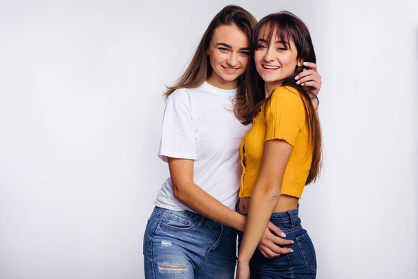 twee meisjes in casual dragen knuffelen en glimlachen. studiofoto. - Foto, afbeelding