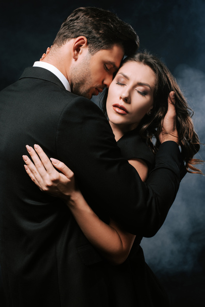 passionate man hugging sensual woman with closed eyes on black with smoke  - Foto, Imagem