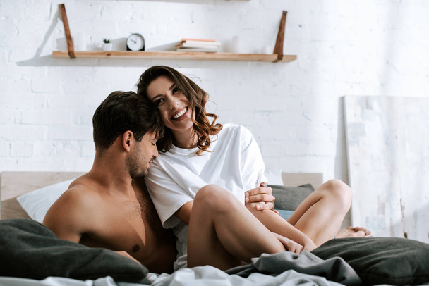 muscular man smiling near happy girlfriend in bedroom  - Foto, afbeelding