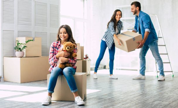 While daughter is playing around with her beloved teddy bear, mother and father have already started to unpack the boxes. - Φωτογραφία, εικόνα
