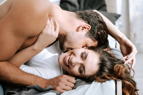 passionate man kissing happy girl lying on bed  - Photo, Image