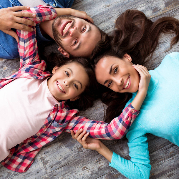 Happy young family of three lying on floor  - Zdjęcie, obraz