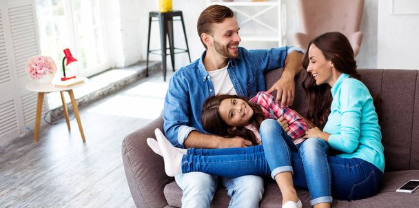 Giovani genitori felici con una figlia piccola sul divano nel loro appartamento
  - Foto, immagini