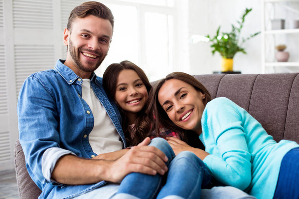 Happy young parents with a little daughter on sofa in their apartment  - Foto, immagini